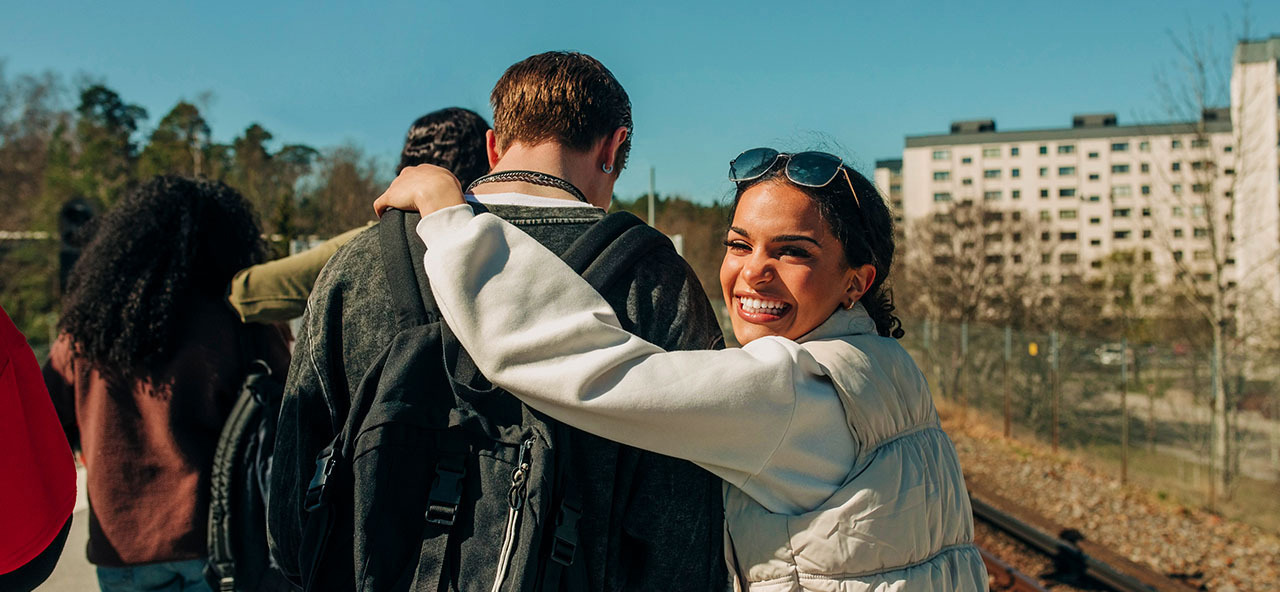 Leende kvinna kramar en vän i en grupp som går utomhus i solen.